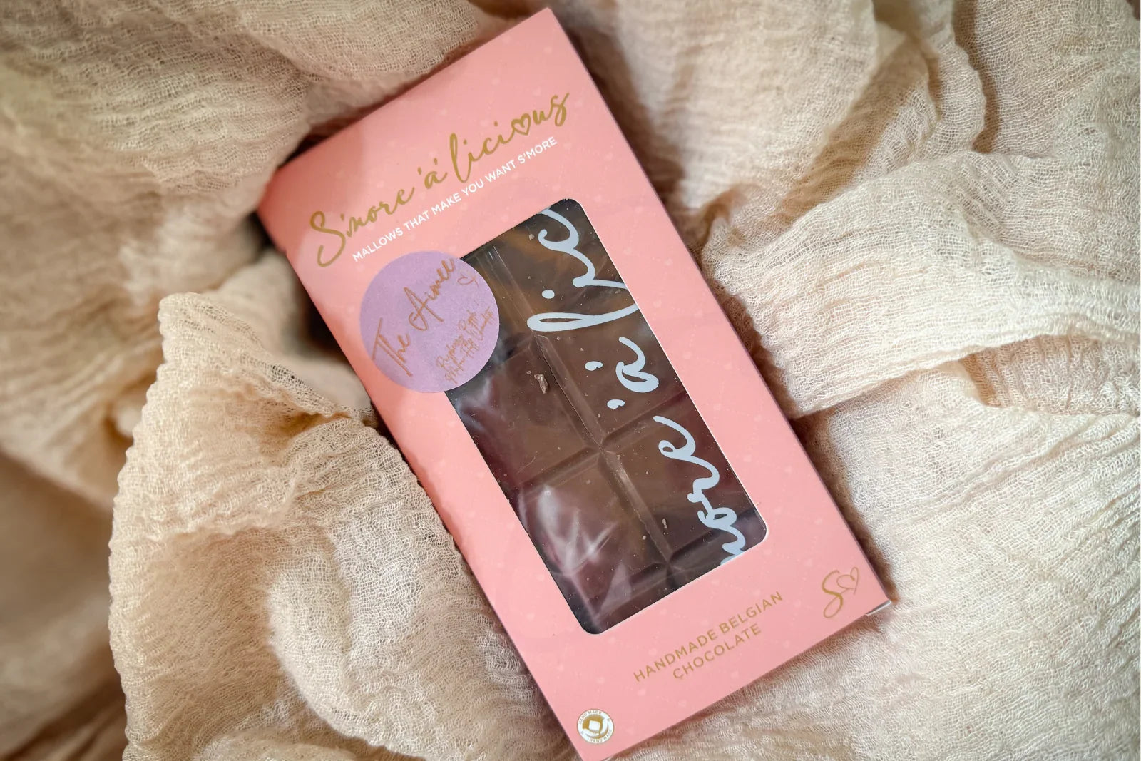 Pink box of chocolate marshamallow bar with 'S'more'a'licious' branding on a soft fabric background