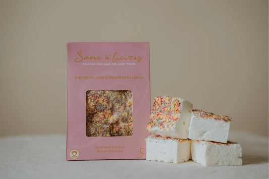 Box of marshmallows with a stack of marshmallows with sprinkles on a neutral background