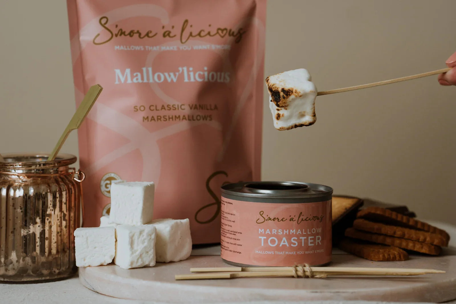 S'more-making setup with marshmallows, a toaster, and packaging on a wooden board.
