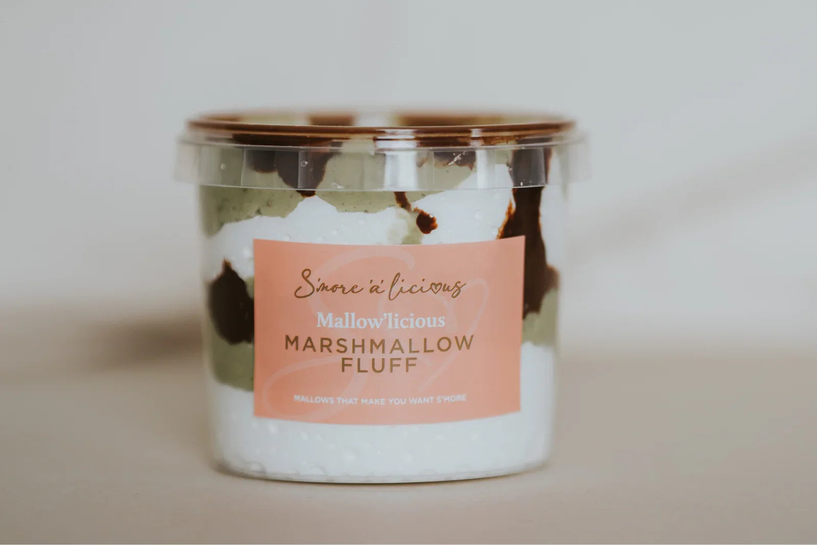 Jar of marshmallow fluff with pistachio and milk chocolate with a pink label on a neutral background