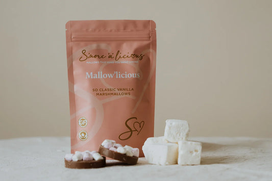 Pink packaging of 'Mallow'licious' marshmallows with marshmallows and hot chocolate on a beige background