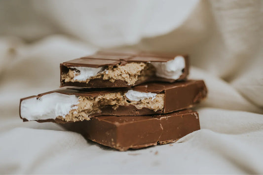Stack of chocolate-covered bars with marshmallow fluff and kinder bueno spread on a soft fabric background