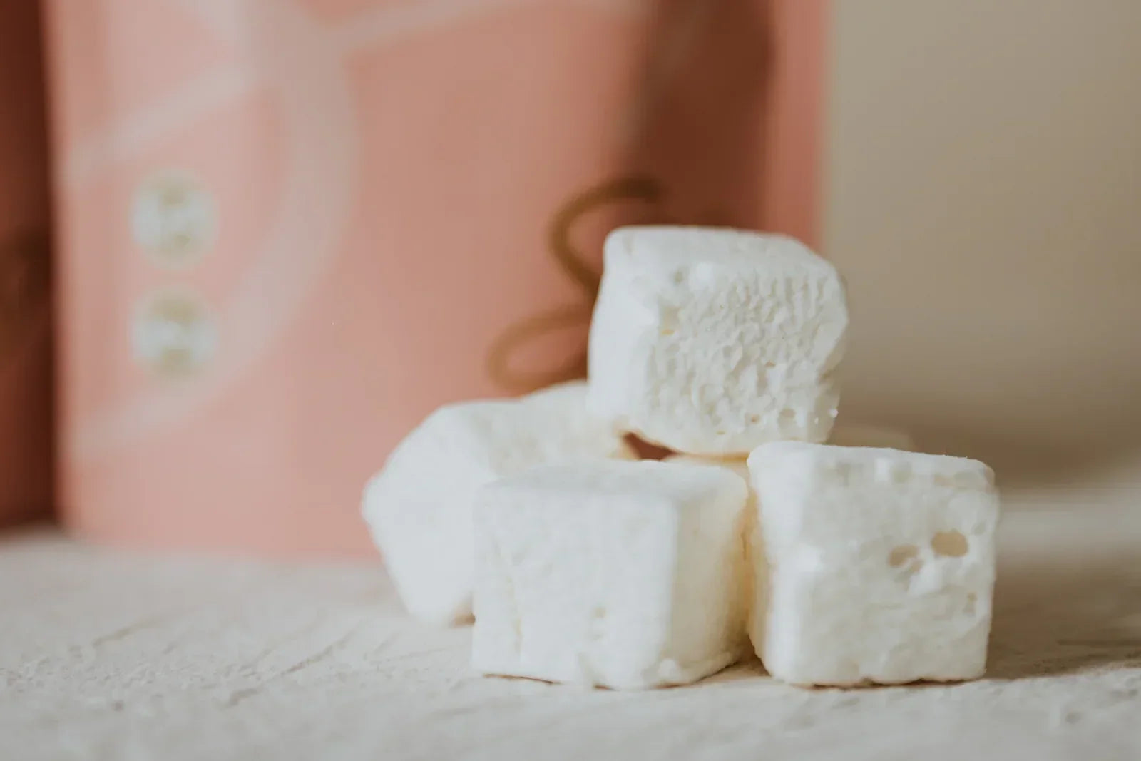 Stack of white marshmallows on a textured surface with a blurred pink background