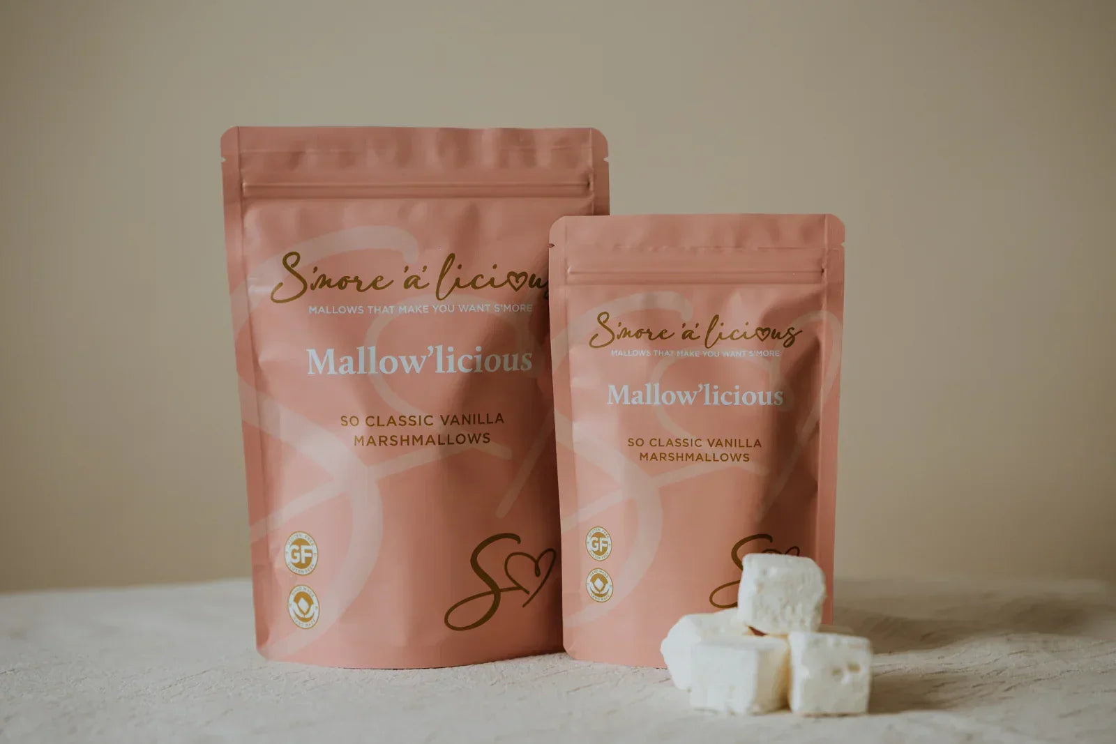 Two pink packages of 'Mallowlicious' marshmallows on a beige surface.