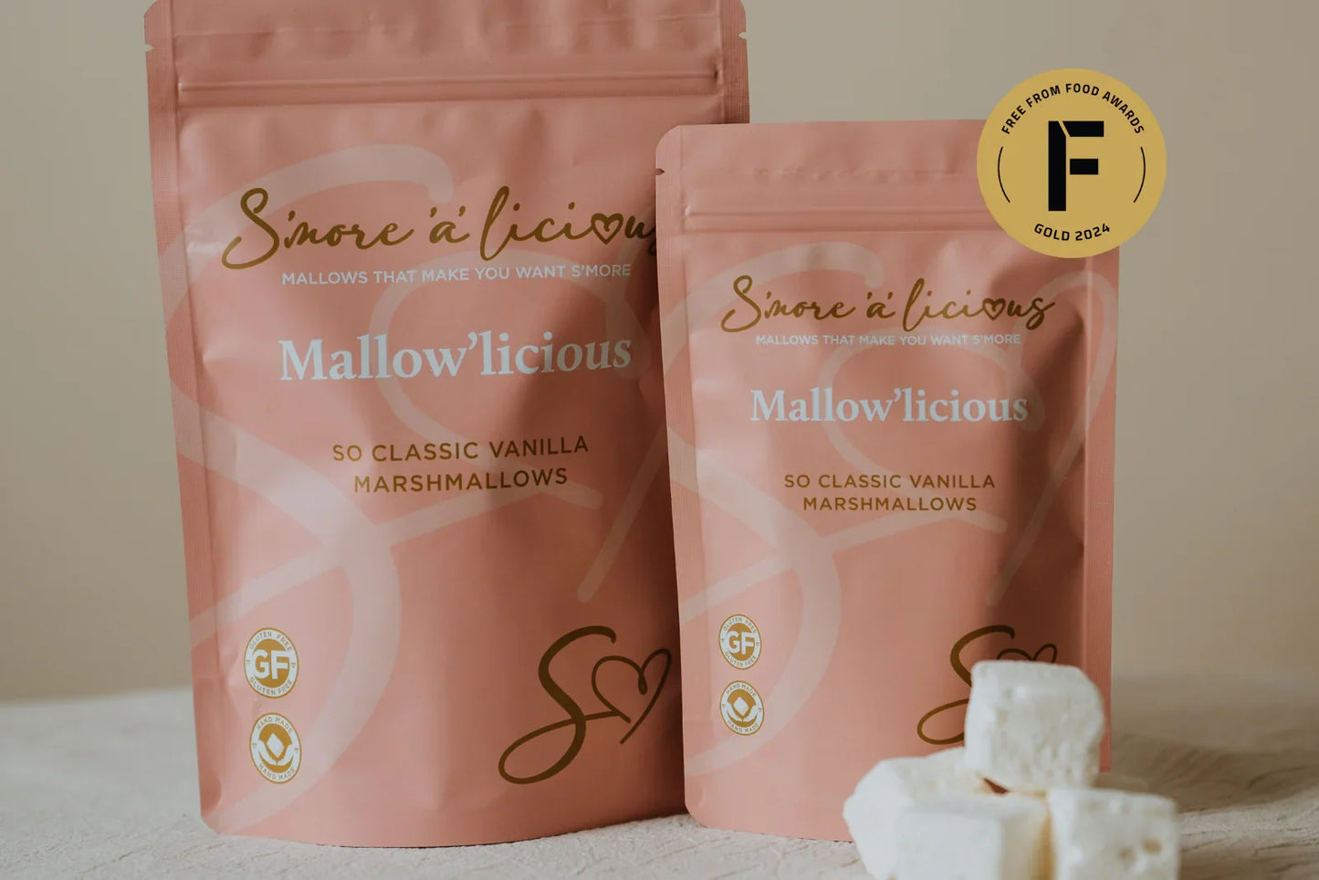 Two pink packages of 'Mallow'licious' marshmallows with a gold award badge on a beige background.
